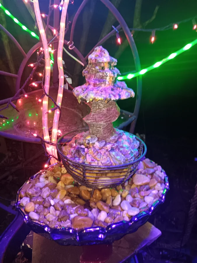 A tiered fountain built from salvaged materials, lit in pink and green